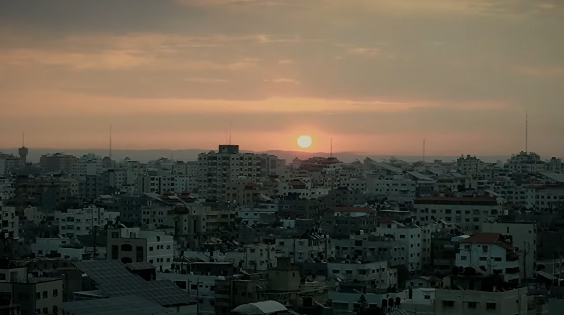 Sunset over a dense urban skyline with low-rise buildings and antennas along the horizon.